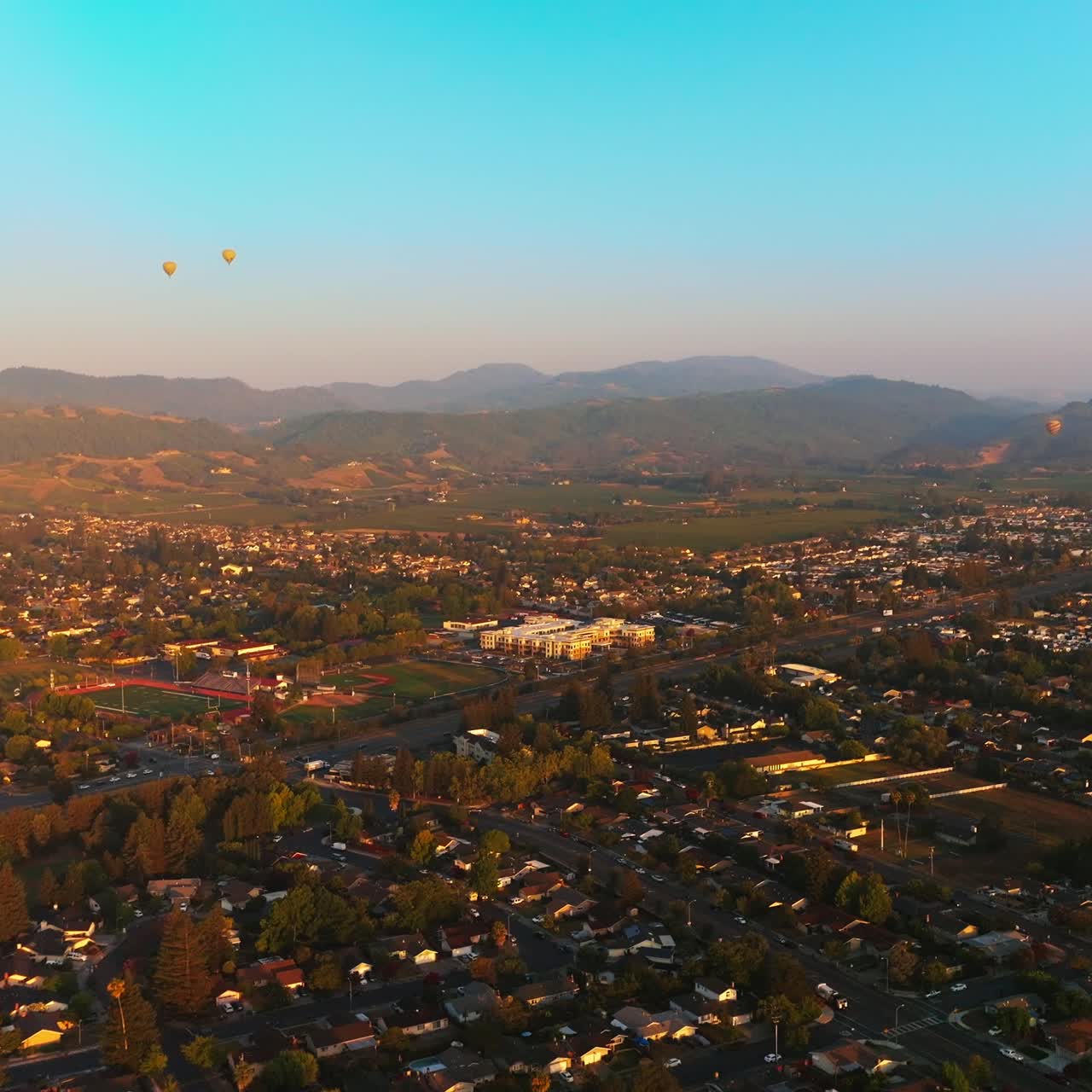Hot air balloons flying over the beautiful city. Sunlit scenery of Napa, California, USA at the backdrop of hazy mountains. Top view