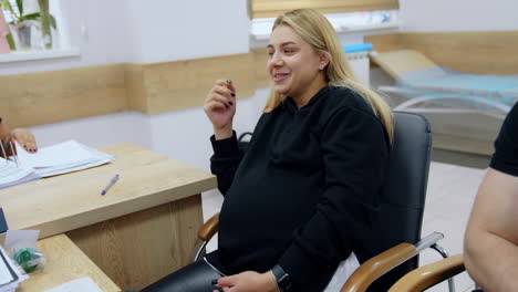 smiling blonde caucasian pregnant lady talking to a doctor. woman speaks and gestures with her hand.