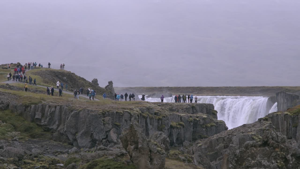 Tourists admire the stunning Godafoss waterfall from a scenic viewpoint on a cloudy day
