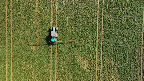 fotografía aérea de arriba hacia abajo de un tractor rociando en un campo verde exuberante con líneas de pista distintas