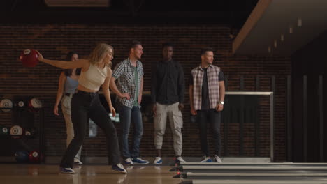 a young blonde woman makes the final throw with a bowling ball and wins the game with the support and joy of her friends of different nationalities. rejoice and celebrate the victory