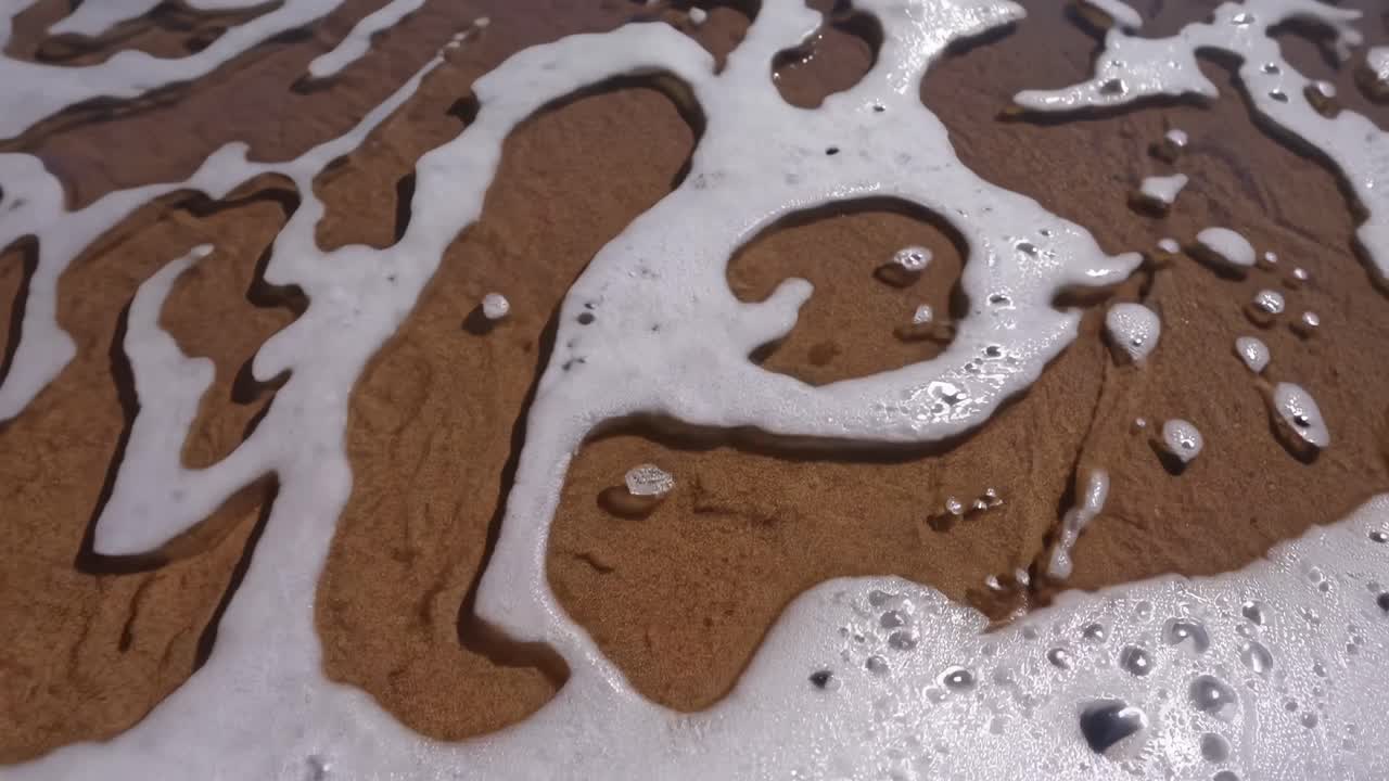 Video sereno di una spiaggia ripreso dal basso, che mostra onde delicate che lambiscono la riva.