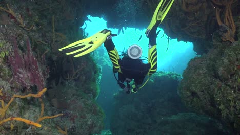 female scuba diver girl diving trough cave in the carribean towards the exit into the open sea