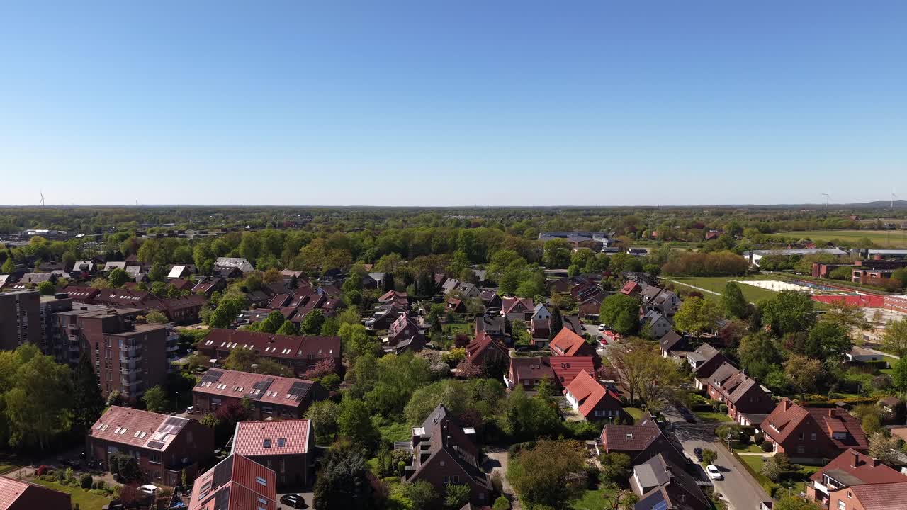 Luchtopname van een typisch Duitse buitenwijk met rijtjeshuizen van rode baksteen, appartementencomplexen en straten met bomen onder zonnige lenteluchten. Rustige woonwijk met klassiek Europa