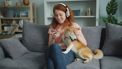 pretty lady enjoying music in headphones using smartphone stroking dog at home