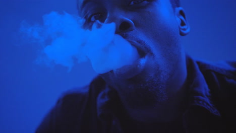 african american man blowing smoke from a hookah in a blue lit room