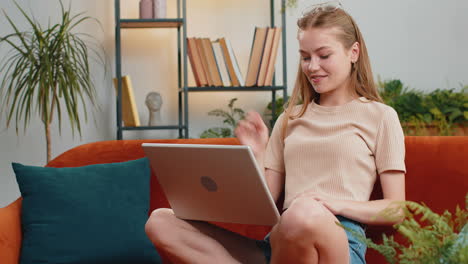 woman sitting on home couch, looking at camera, making video conference call with friends or family