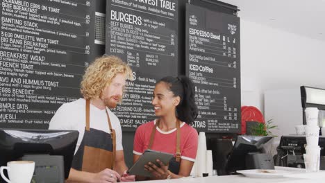 Happy-diverse-male-and-female-baristas-talking-and-using-tablet-behind-counter-in-cafe