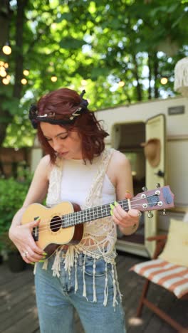 woman playing ukulele outdoors by a camper trailer