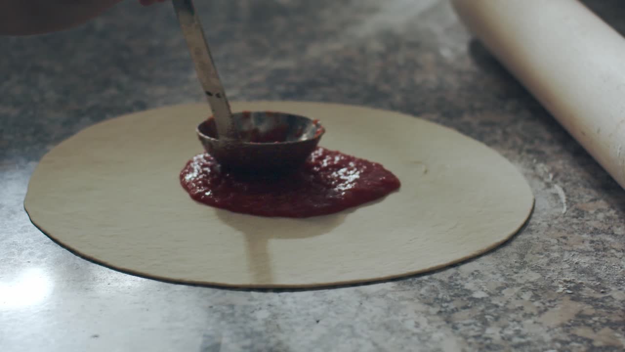 Crop chef smearing tomato sauce on pizza