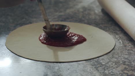 crop chef smearing tomato sauce on pizza