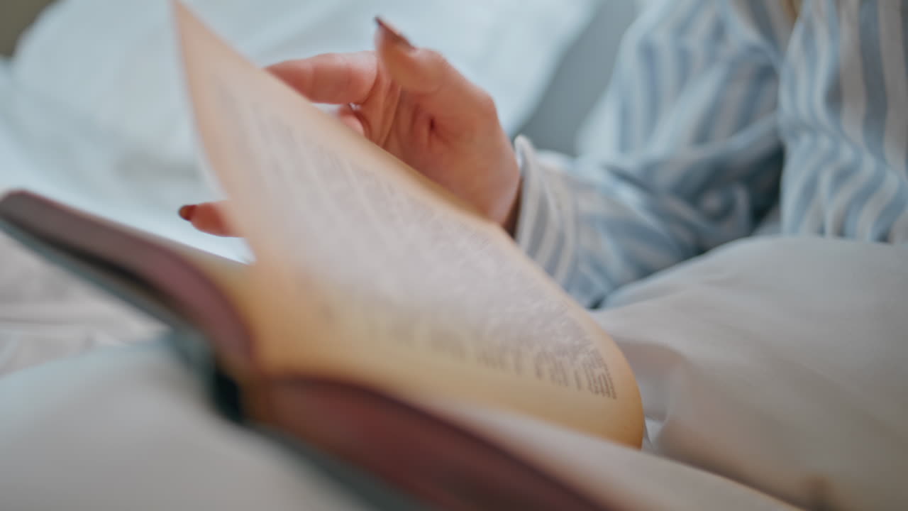 Lady hands holding book in bedroom interior closeup. Unknown woman turning pages