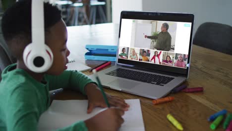 schoolboy using laptop for online lesson at home, with diverse teacher and class on screen
