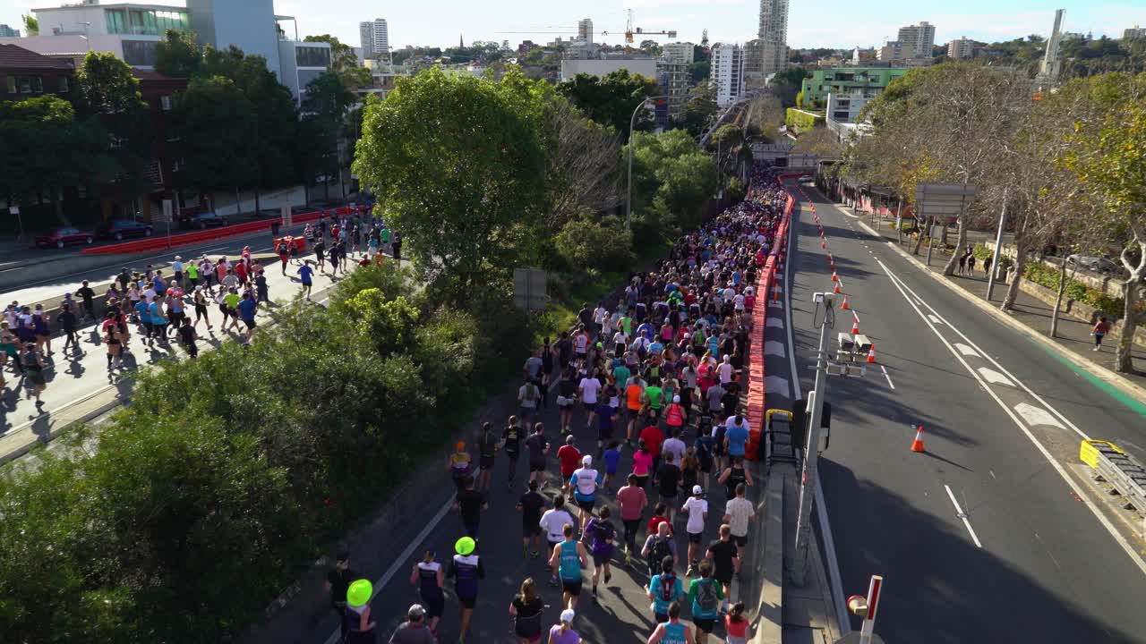 Smooth shot of people participating in a running contest. The race takes place on the streets in the middle of the city. Bright, sunny day.