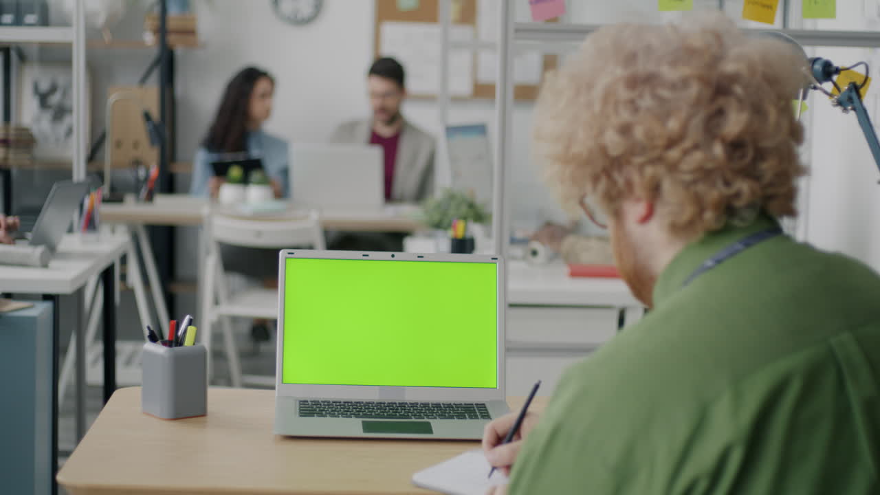 Office scene with green screen laptop and people working