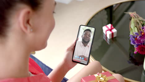 Mujer-Caucásica-Sosteniendo-Regalo-Y-Teléfono-Inteligente-Con-Un-Hombre-Afroamericano-En-La-Pantalla