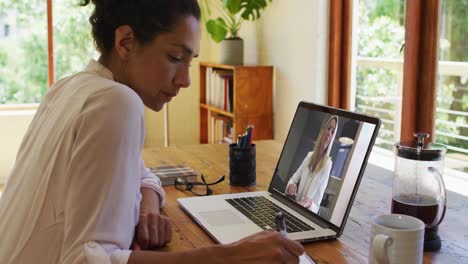 Mixed-race-businesswoman-sitting-at-desk-using-laptop-having-video-call-with-female-colleague