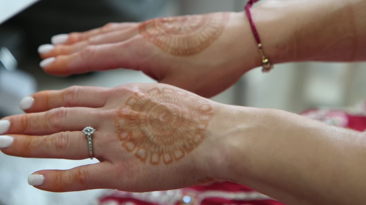 Primo piano delle mani di una sposa che mostra disegni all'henné. La sposa ruota le mani per rivelare l'intricata arte mehndi sia sul davanti che sul retro, catturando la preparazione tradizionale del matrimonio.