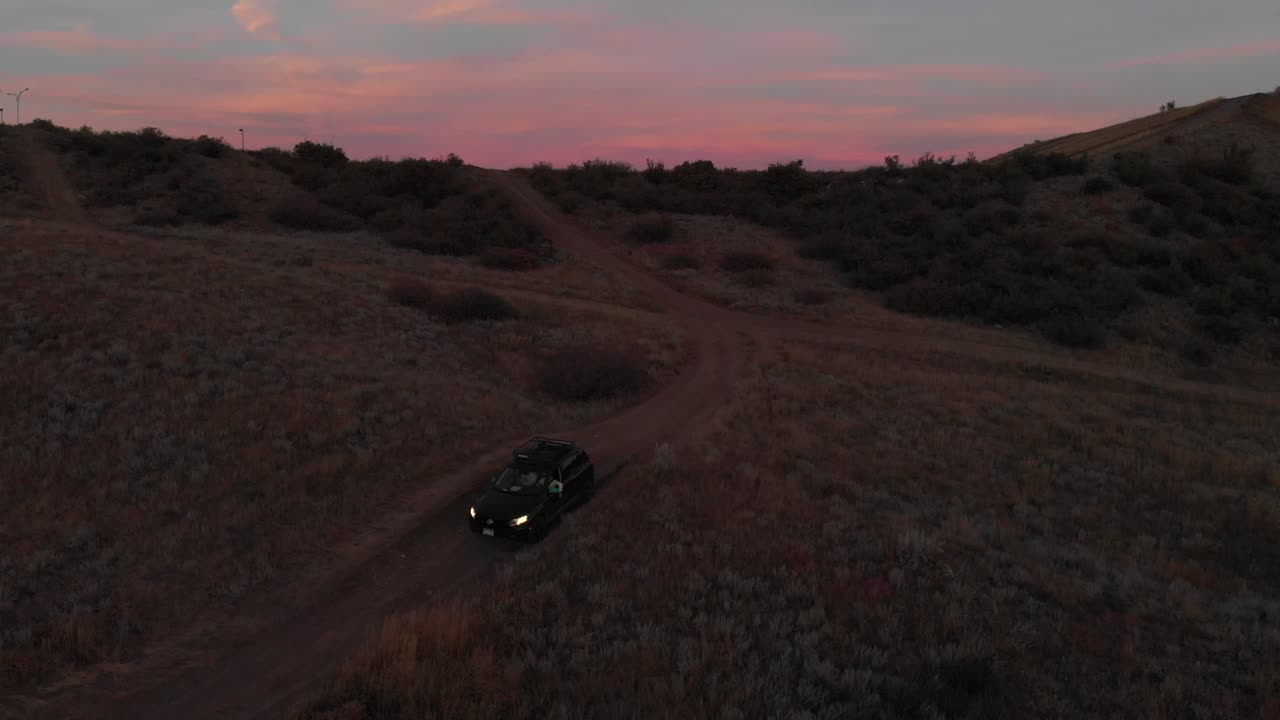 Cielo drammatico rosa e blu mentre una ripresa aerea in allontanamento segue un SUV al crepuscolo
