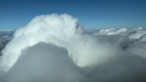 Immersive pilot POV FPV flying over a sea of fluffy clouds with a blue sky in a sunny day. Aerial footage taken from an airplane cockpit overflying and penetrating a clouds. 4K 60FPS