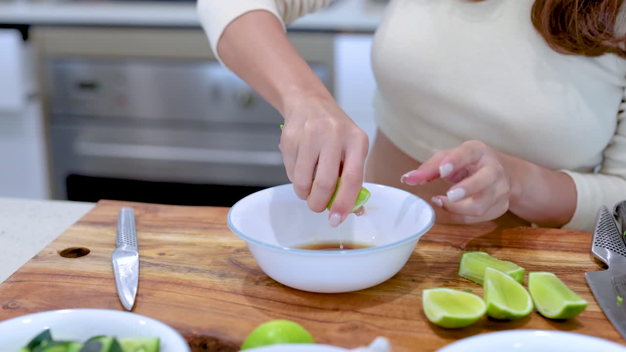 A person squeezes lime juice into a bowl on a wooden cutting board in a well-lit kitchen