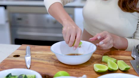 a person squeezes lime juice into a bowl on a wooden cutting board in a well-lit kitchen