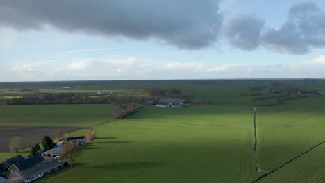 aerial of a distant farm surrounded by green meadows