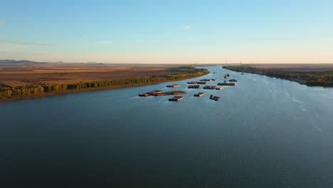 Aerial-tracking-wide-shot-of-distant-anchored-barges-on-a-big-blue-river,-clear-sunny-day,-4K50Fps