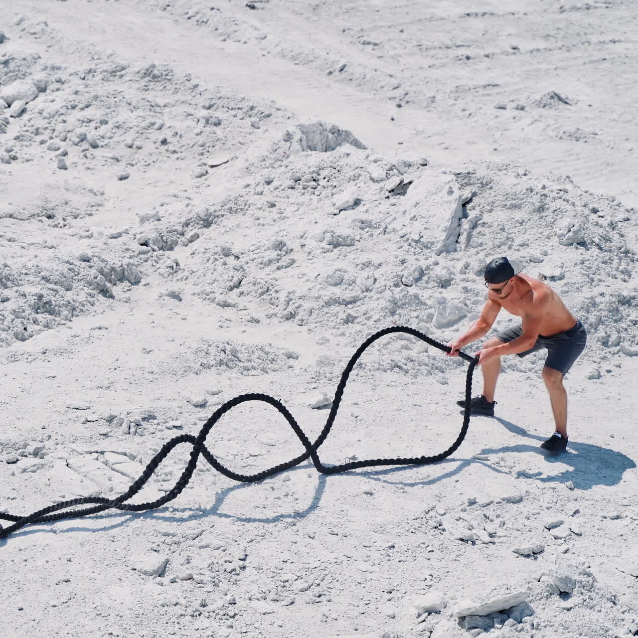 Athletic young man working out with battle ropes. Bodybuilder posing outdoors.