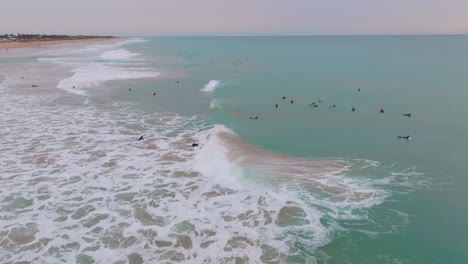 las olas chocando, extendiendo una hermosa niebla oceánica sobre los surfistas al atardecer, órbita aérea