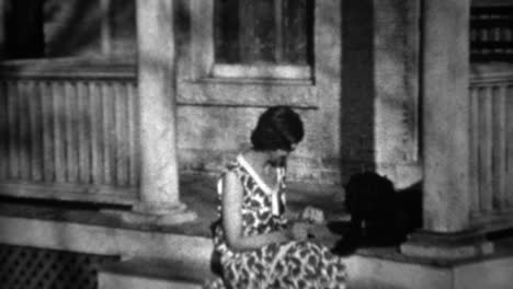 1934: women plays with black dog on front stoop house porch.