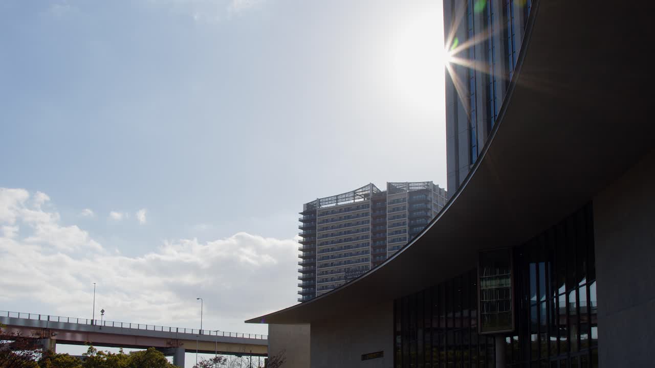 Raios de sol irrompem por trás de um arranha-céu, trânsito em rodovia elevada na cidade