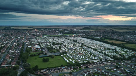 Aerial-drone-view-of-Skegness-town-by-the-sea-at-sunset,-with-holiday-park,-beach,-and-caravans