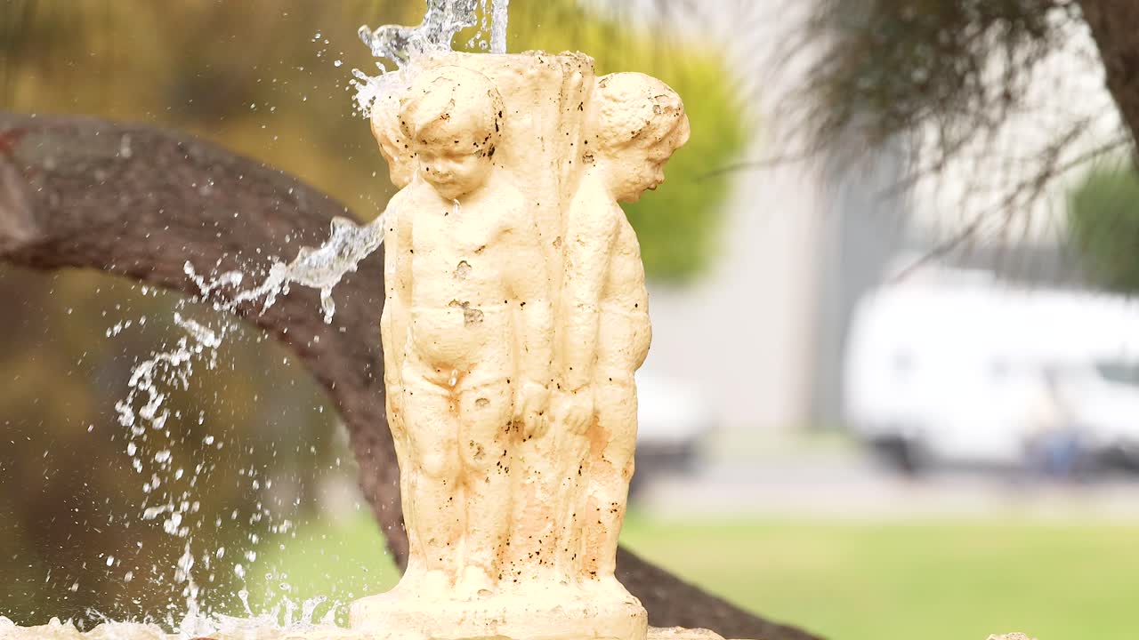A stone fountain statue with flowing water, set against a natural backdrop, captured in bright daylight