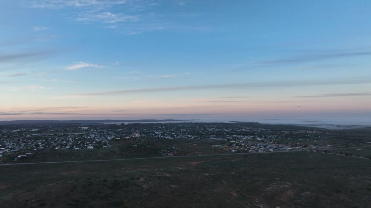 Amplia vista aérea de dron sobre las afueras de Broken Hill y el vasto interior circundante bajo un suave cielo pastel al amanecer