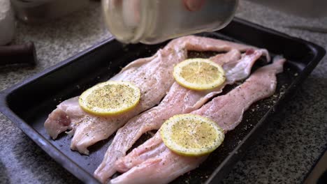espolvorear especias sobre filete de merluza fresca con rodajas de limón en un molde para hornear