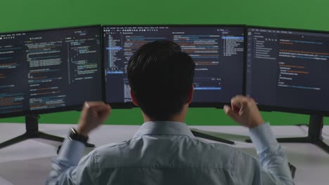 Back View Of Happy Asian Man Developer Celebrating And Dancing While Write Code With Multiple Computer Screens In Green Screen Studio