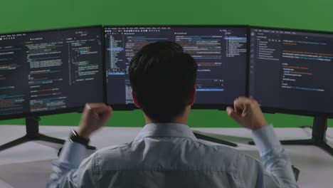 back view of happy asian man developer celebrating and dancing while write code with multiple computer screens in green screen studio