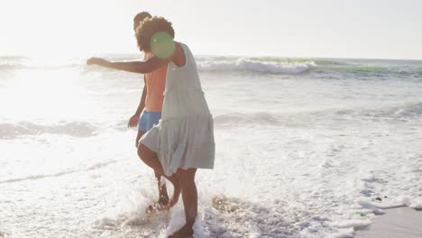 una pareja afroamericana sonriente cogida de las manos y caminando por una playa soleada