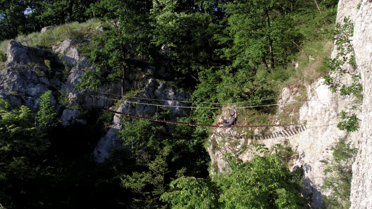 turista que cae mientras cruza un puente colgante de madera pero es salvado por un engranaje de via ferrata