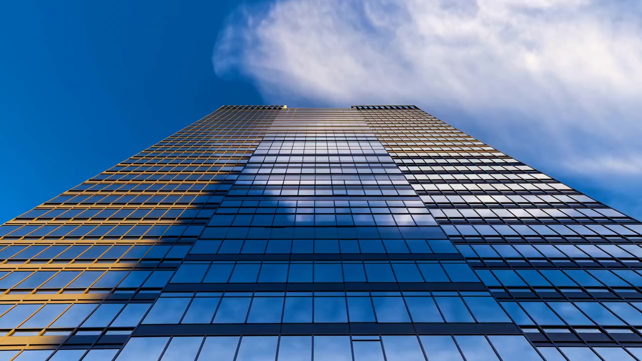 El fotograma central de la secuencia muestra un rascacielos alto de cristal visto desde un ángulo bajo, con ventanas reflectantes, paneles en cuadrícula y un cielo azul vívido.