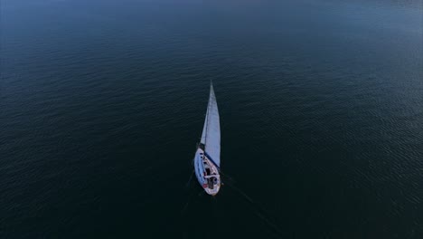 Aerial-flying-over-sailboat-at-sunset-on-calm-water-of-Lake-Maggiore,-Italy