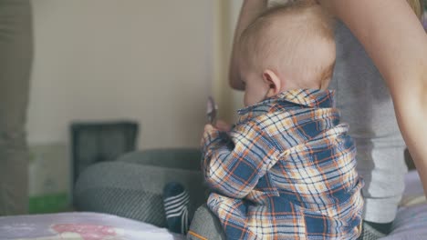 Süßer-Junge-In-Warmer-Kleidung-Spielt-Mit-Dem-Löffel-Von-Mama-Auf-Dem-Bett