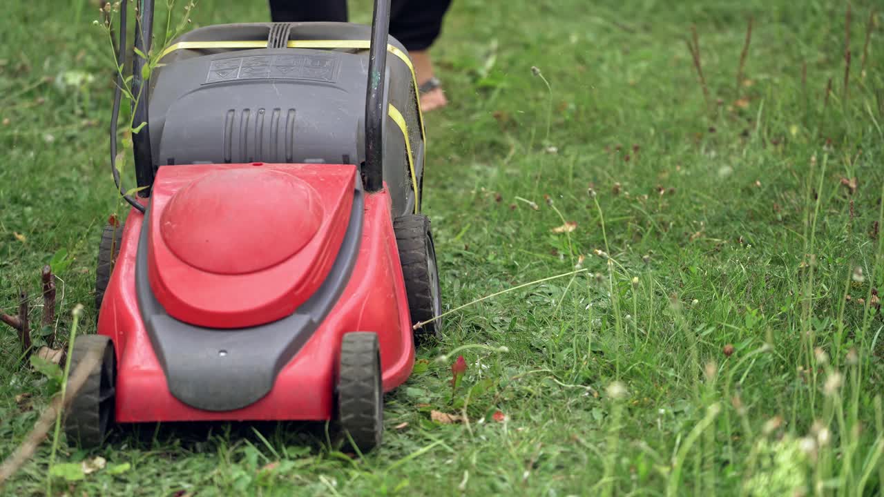 Gardening activity. Green grass in the garden and a worker with lawn mower. Electric machine for mowing grass. Close-up.
