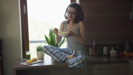 Young-woman-sitting-on-table-and-eating-breakfast