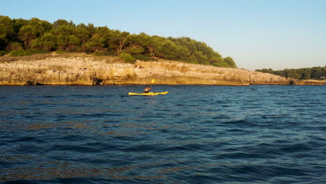 hombre en kayak en el mar adriático al atardecer cerca de la playa de rocas de gaviota en pula, croacia