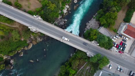 Aerial Birds Eye view looking down onto bridge with cars driving past above beautiful flowing blue river - Neretva River, Mostar, Bosnia and Herzegovina