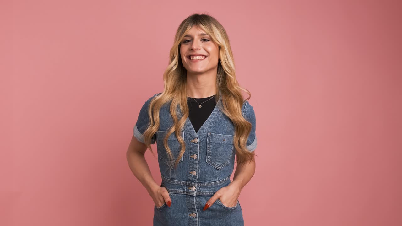 Happy transgender woman in denim dress against pink background