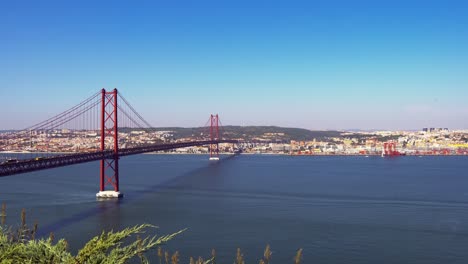 amazing architecture of the 25 de abril suspension bridge and passing traffic at daytime with the view of lisbon in the background, portugal
