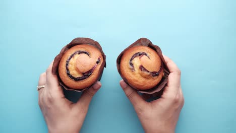 hands holding two blueberry muffins on a blue background